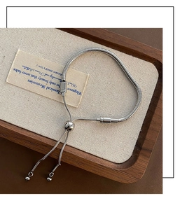 Detail of adjustable silver snake chain bracelet with sliding clasp on wooden tray