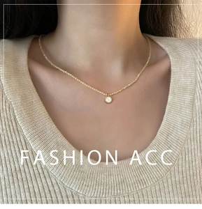 Detail of beaded necklace with a gold-rimmed circular pendant on a rib-knit sweater