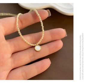 Detailed close-up of champagne beaded necklace with a white circular pendant and gold frame