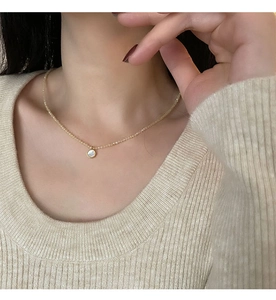 Close-up of a delicate gold chain necklace with a round white shell pendant and small beads