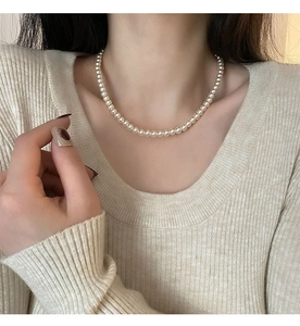 Gros plan d'un collier de perles crème monocouche porté au cou d'un modèle