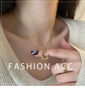 Detailed view of a gold G-letter pendant with a green gemstone on a beaded chain necklace