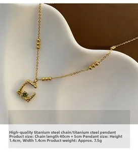 Macro shot of gold stainless steel necklace featuring a C-shaped pendant with a green gemstone