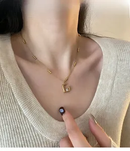 Detail view of a gold square frame necklace with zircon on a model wearing beige knitwear
