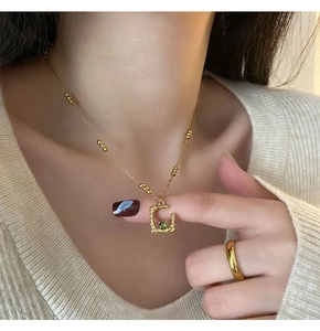 Detailed view of a gold C-letter necklace with green gemstone on a model wearing beige sweater