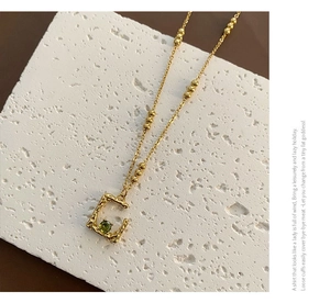Detail of C-shaped gold necklace pendant with textured metal and green faceted gemstone