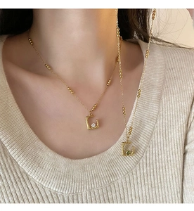 Detail of irregular square necklaces with white and green gems on a beige knit sweater