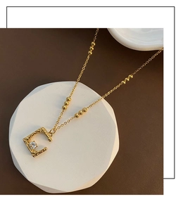 Detail of gold lava-textured C pendant necklace with a small zircon on a stone stand
