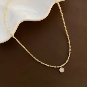 French zircon bead necklace with a golden shell pendant on a vintage leather desk