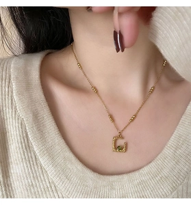 Detail of gold necklace with irregular square pendant and green gemstone on a model