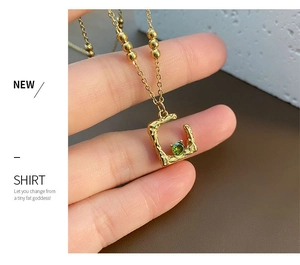 Macro view of gold-plated irregular square pendant with green gemstone and beaded chain