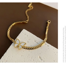 Close-up of golden Cuban chain bracelet with white butterfly charm on stone