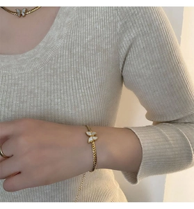 Detailed view of a gold chain necklace with a white butterfly pendant on a beige knit sweater