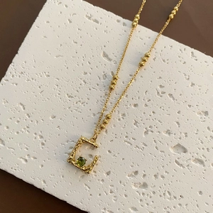 Golden irregular C-shaped pendant necklace with green gemstone and beaded chain