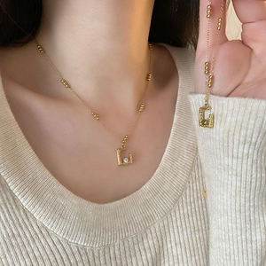 Gold-tone necklace and bracelet set with G-shaped charms and green gemstone accents