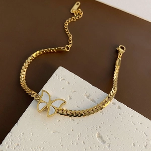 Golden Cuban chain bracelet with white shell butterfly pendant on a stone stand