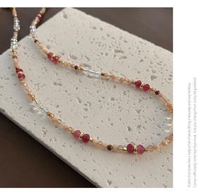 Macro detail of beaded necklace with red and champagne beads on textured stone