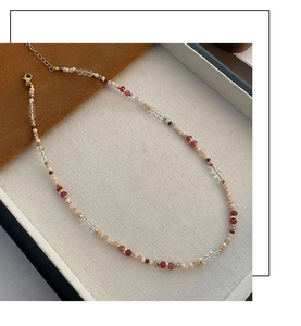 Detail of beaded necklace with red and pink faceted beads and gold-tone lobster clasp