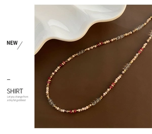 Detail of beaded necklace with red and pink stones on a ceramic plate with brown leather