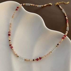 Handcrafted asymmetric beaded necklace with pink and red gems on a white ceramic tray