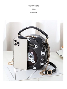 Detail of round black cat print crossbody bag next to a smartphone for size comparison