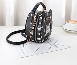 Detail of a round black leather crossbody bag featuring a cute cat pattern and chain strap