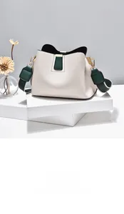 Close-up of white lychee textured bag with green leather trim and gold hardware on a pedestal