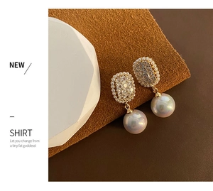 Detail of zircon earrings with gold plating and large round pearl pendant on leather