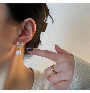Detail of elegant pearl earrings with zircon inlay and golden minimalist ring on model