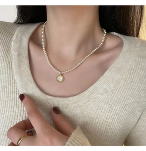 Perlenkette mit weißem Muschelanhänger auf Model mit beigem Strickoberteil