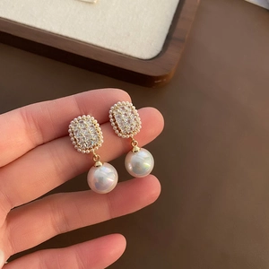Elegant gold zircon earrings with large round pearls shown held in hand