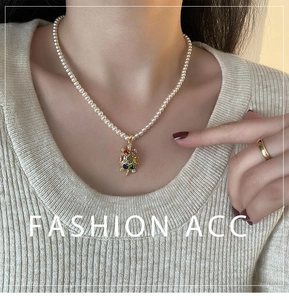 Détail de collier de perles avec pendentif tortue dorée serti de zircons multicolores