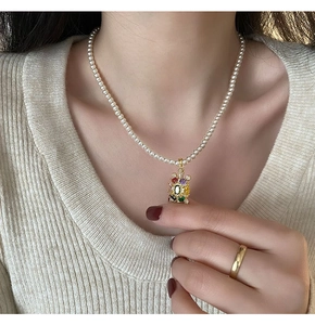 Détail du collier en perles blanches avec pendentif tortue aux pierres colorées
