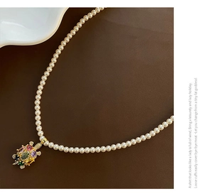 Gros plan du collier de perles avec pendentif tortue serti de pierres colorées