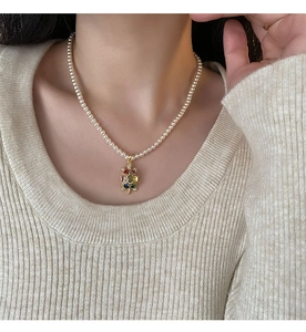 Détail d'un pendentif tortue avec zircons colorés sur un collier de perles blanches