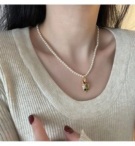 Détail d'un collier de perles avec pendentif tortue et zircons colorés porté par un mannequin
