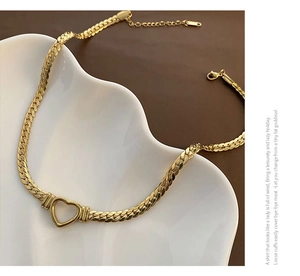 Détail du collier cœur doré avec chaîne serpent plate posé sur une assiette blanche
