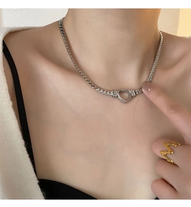 Détail du collier cœur en argent à chaîne plate et bague dorée ondulée sur un modèle
