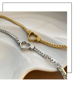 Détail de chaînes serpent plates or et argent avec pendentif cœur ajouré sur plateau