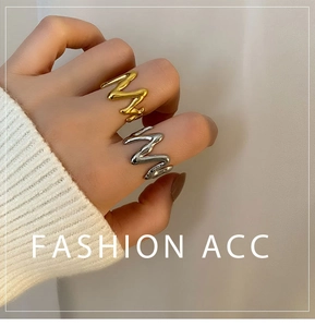Macro detail of wave-shaped geometric rings in gold and silver finish on finger