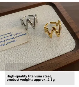 Detail view of wavy stainless steel rings in gold and silver finish on a wooden tray