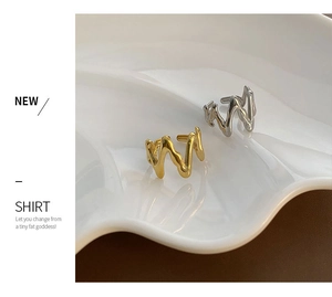 Detailed view of wave-shaped ear cuffs in gold and silver on a white ceramic tray