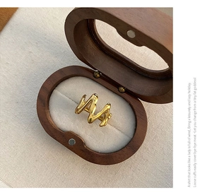 Close-up of golden M-shaped wavy stainless steel ring in premium wood jewelry box
