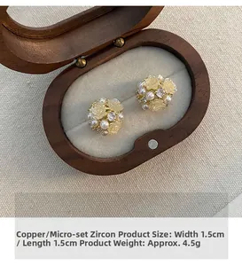 Nahaufnahme von Blumen-Zirkon-Ohrsteckern mit Perle auf einer vintage Holz-Schmuckschatulle