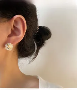 Nahaufnahme eleganter Perlenohrstecker mit Kristallen auf goldener Basis an einem Model