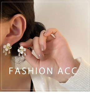 Detail of white camellia earrings with gold trim and hanging zircon stones on model