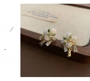 Detailed view of white camellia flower earrings with golden butterfly and zircon tassels