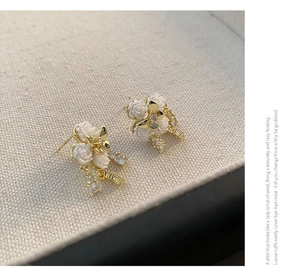 Macro view of white camellia earrings with gold butterfly accents and zircon inlays
