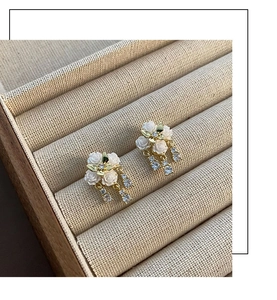 Detail of white camellia earrings with gold leaves and hanging zircon crystals