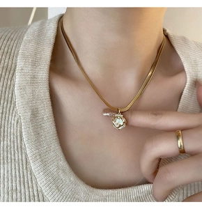 Detail of a gold shell pendant necklace with mother of pearl on a snake chain and knit sweater